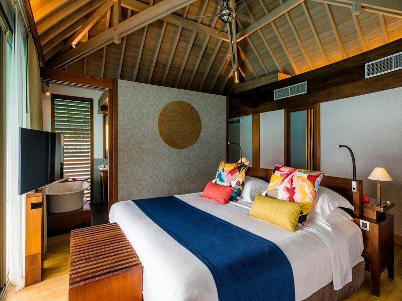 Bett im Hotelzimmer des InterContinental Bora Bora Resort and Thalasso Spa mit bunten Kissen und Decken.