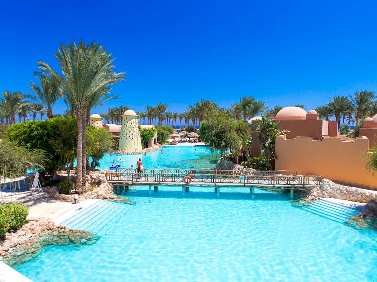 Ein großer Poolbereich des Grand Makadi Hotels mit einer Brücke und mehreren Palmen im Hintergrund.