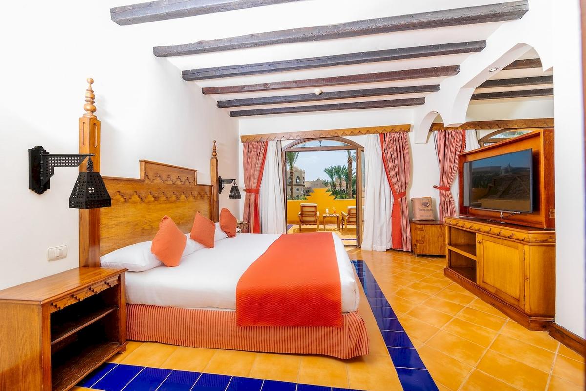 Ein Schlafzimmer im Grand Makadi Hotel mit einem großen Bett, Kissen und einem Fernseher.