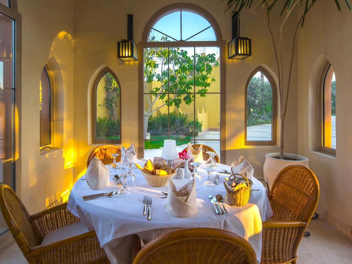 Essenbereich im Grand Makadi Hotel mit Tisch, Stühlen und Blick auf einen Garten.