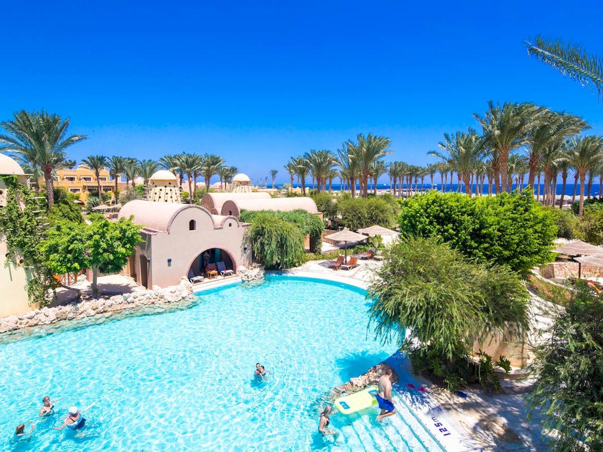 Luftaufnahme des Pools im Grand Makadi Hotel mit Palmen und Meer im Hintergrund.
