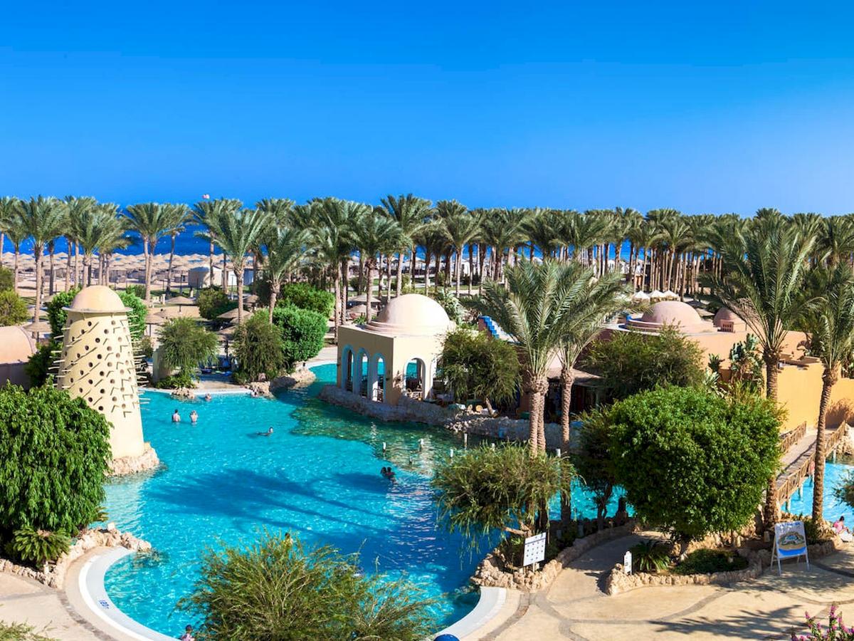 Luftaufnahme des Swimmingpools im Grand Makadi Hotel mit mehreren Schwimmern und tropischen Bäumen.