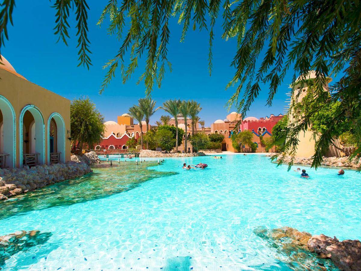 Grand Makadi Hotel zeigt eine große Poollandschaft mit mehreren Schwimmern unter blauem Himmel.