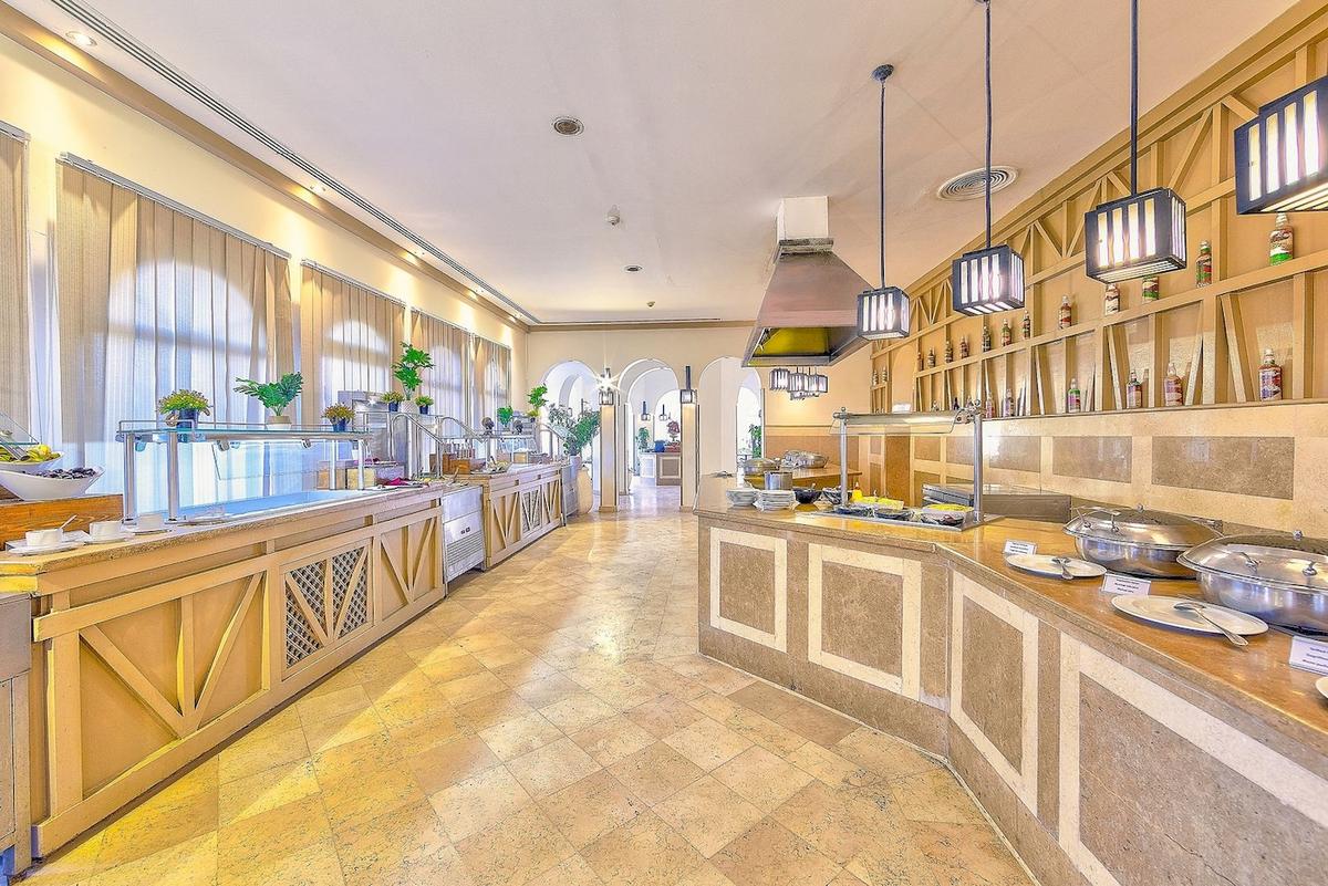 Innenansicht des Speisesaals im Grand Makadi Hotel mit langen Tischen, Buffets und hängenden Lampen.