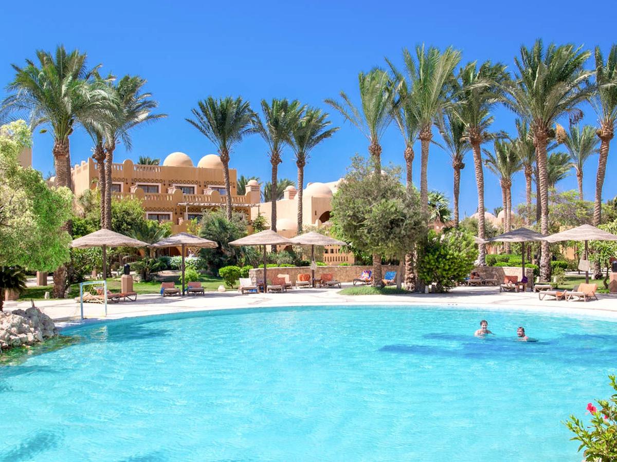Ein Swimmingpool mit mehreren Sonnenschirmen und Liegestühlen am Grand Makadi Hotel