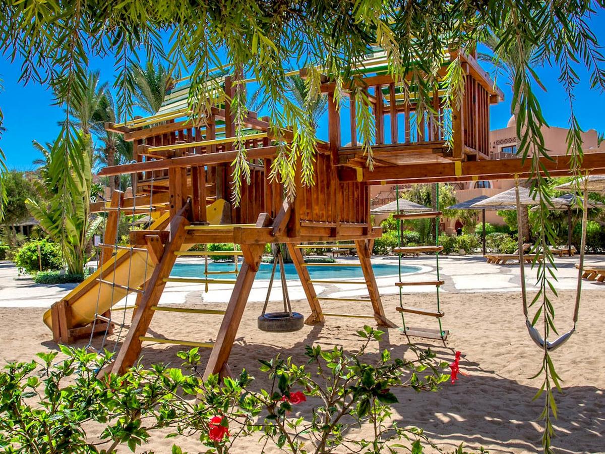 Ein großer hölzerner Spielplatz mit Rutsche und Schaukeln im Freien am Grand Makadi Hotel.