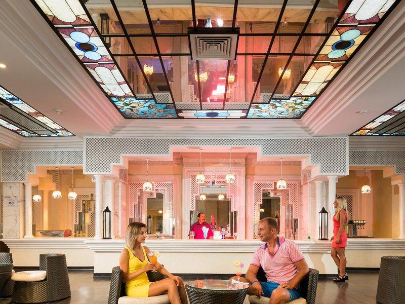 Hotellobby mit beleuchteten Decken und Sofas, wo ein Paar Getränke genießt.