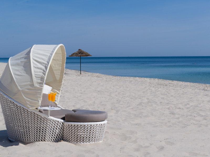 Ein weißer Lounge-Stuhl mit Sonnenschirm auf einem weißen Sandstrand mit Blick auf das blaue Meer.