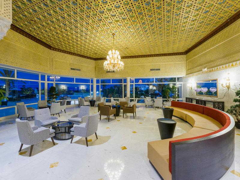 Lobby des JAZ Tour Khalef Hotels mit goldener Decke, Kronleuchter, Sofas und Tischen.