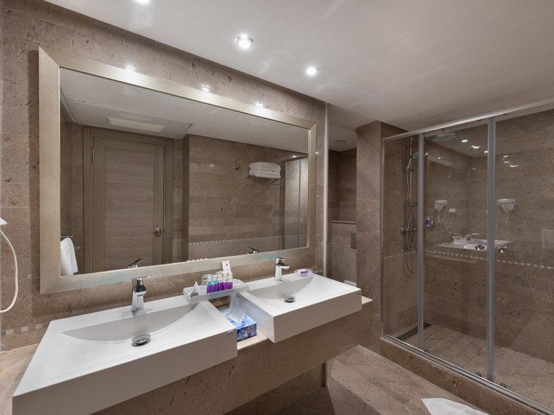 Badezimmer mit zwei Waschbecken, einem großen Spiegel und einer Glasdusche im JAZ Tour Khalef Hotel