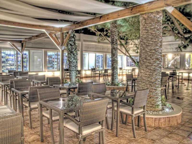 Innenansicht des Restaurants im Sahara Beach AquaPark Resort mit Tischen, Stühlen und Palmen.