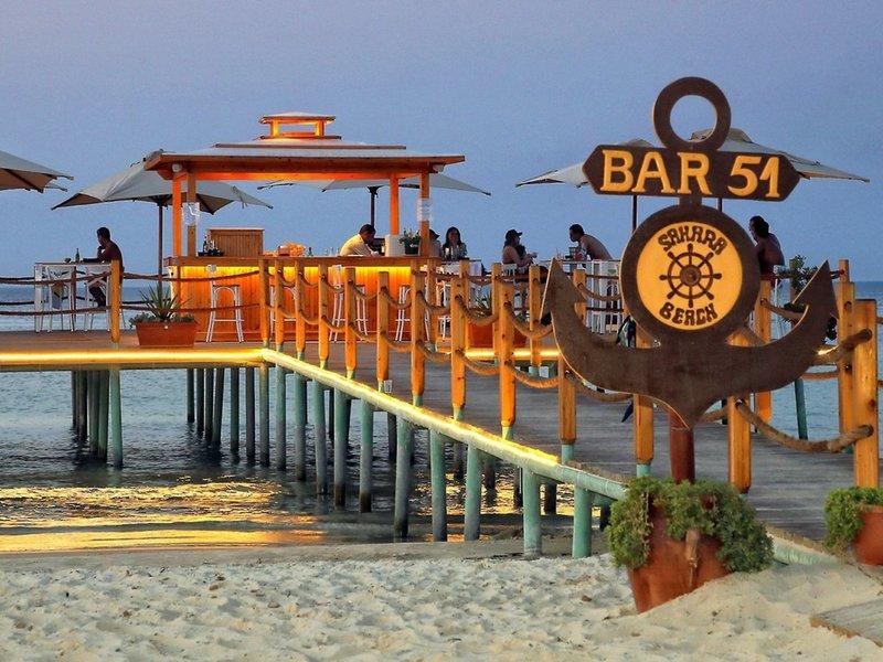Abendansicht des Bars am Wasser im Sahara Beach AquaPark Resort mit Gästen und Palmen