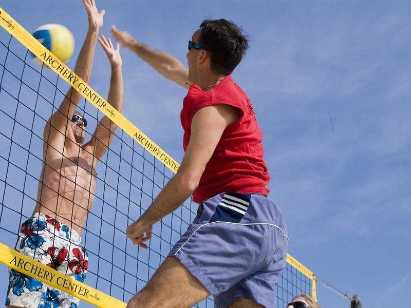 Zwei Männer spielen Volleyball am Strand vor einem gelben Netz.