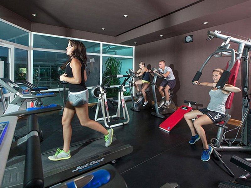 Fitnessstudio im Sahara Beach AquaPark Resort mit mehreren Personen, die auf Laufbändern und anderen Geräten trainieren.
