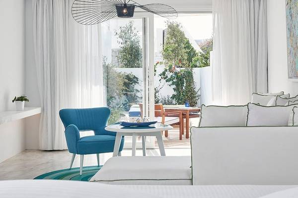 Innenansicht der Myconian Ambassador Relais & Chateaux Suite mit weißem Interieur, blauem Stuhl, weißem Tisch und Wohnzimmermöbeln.