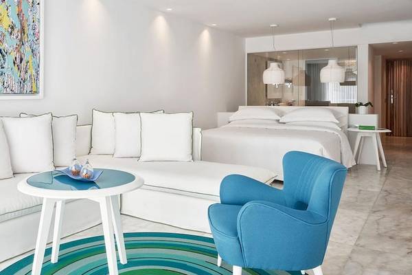 Suite-Innenbereich im Myconian Ambassador Relais & Chateaux Hotel mit weißen Möbeln und einem modernen Kunstwerk.