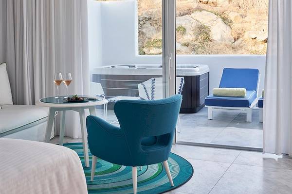 Innenansicht der Myconian Ambassador Relais & Chateaux Suite mit Bett, Sofa, Tisch, Weinglas und Whirlpool.