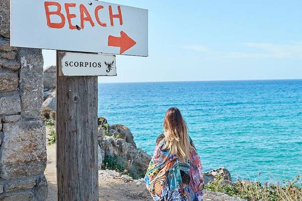 Frau steht am Strand vor einem Schild mit der Aufschrift Beach und einem Pfeil, der auf das Meer zeigt.