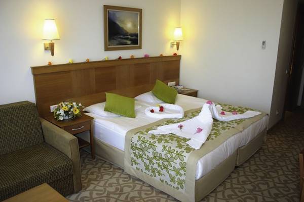 Hotelzimmer mit einem Doppelbett, Blumen, grünen Kissen, Nachttischen und Wandlampen.