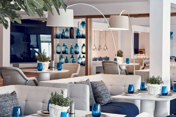 Hotel-Lounge des Myconian Ambassador Relais & Chateaux mit weißen Möbeln, blauen Gläsern und Pflanzen.