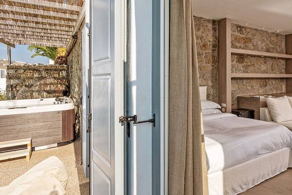 Myconian Ambassador Relais & Chateaux Zimmer mit Schlafbereich und Sofa.