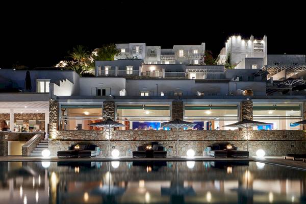 Myconian Ambassador Relais & Chateaux Hotel nachts beleuchtet mit Pool und Sonnenschirmen.