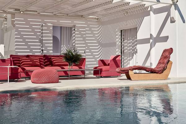 Poollounge im Myconian Ambassador Hotel mit roten Möbeln und einem weißen Gebäude.