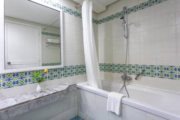 Badezimmer des Djerba Holiday Beach Hotels mit Badewanne, Dusche, Spiegel und Blumenvase.