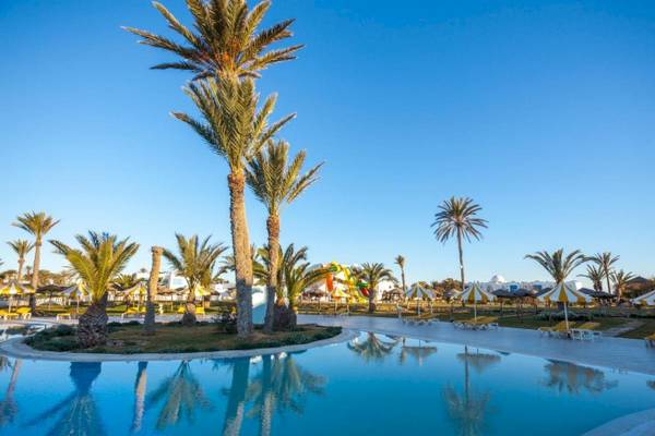 Außenpoolbereich des Djerba Holiday Beach Hotels mit Palmen, Sonnenliegen und gelben Sonnenschirmen.