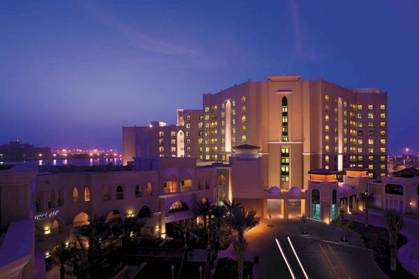 Abendansicht des Traders Hotel Qaryat Al Beri mit illuminierten Fenstern und einer beleuchteten Einfahrt.