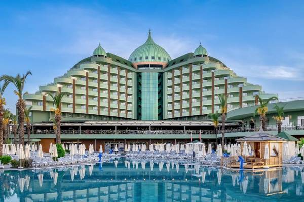 Außenansicht des Delphin Palace Hotels mit großen grünen Kuppeln, Swimmingpool und vielen Liegestühlen.