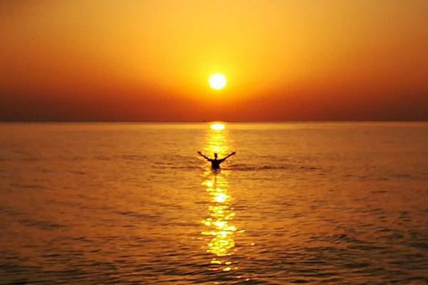 Eine Person schwimmt im Meer während des Sonnenuntergangs, mit der Sonne, die auf dem Horizont untergeht.
