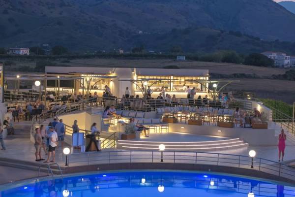 Abend-Pool-Bereich des Georgioupolis Resort Aquapark & SPA mit vielen Gästen und einer Berglandschaft im Hintergrund.