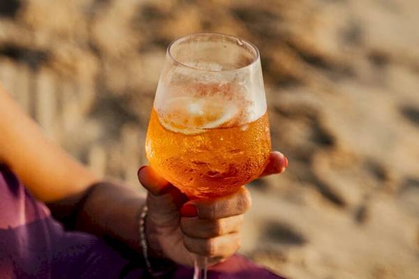 Person hält ein Cocktailglas auf dem Strand