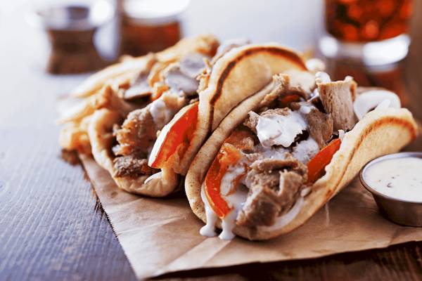 Griechisches Fleisch in Pita-Brot mit Sauce und Beilagen auf einem Holztisch