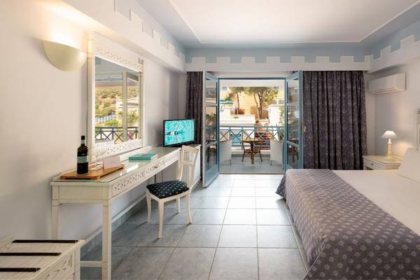 Ein elegantes Hotelzimmer im Mitsis Summer Palace mit Balkon, Bett, Schreibtisch und Fernseher.