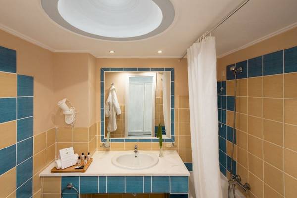 Badezimmer im Mitsis Summer Palace mit blauen und gelben Fliesen, einer Dusche, einem Spiegel und einem Waschbecken.