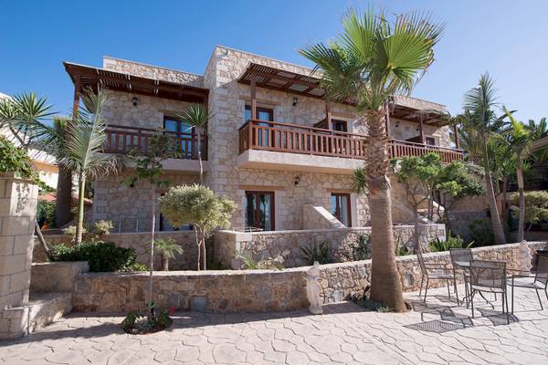 Außenansicht des Cactus Village Hotel & Bungalows mit Steinmauer und Palmen.