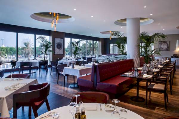 Innenansicht des Restaurants des Radisson Blu Hotel & Resort, Abu Dhabi Corniche mit runden Tischen und roten Sitzbänken.