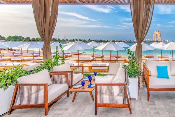 Außenbereich des Radisson Blu Hotel & Resort in Abu Dhabi mit weißen Sonnenschirmen und Möbeln am Strand.