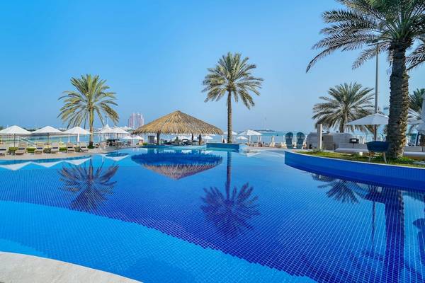Poolbereich des Radisson Blu Hotel & Resort am Abu Dhabi Corniche mit Sonnenliegen und Palmen
