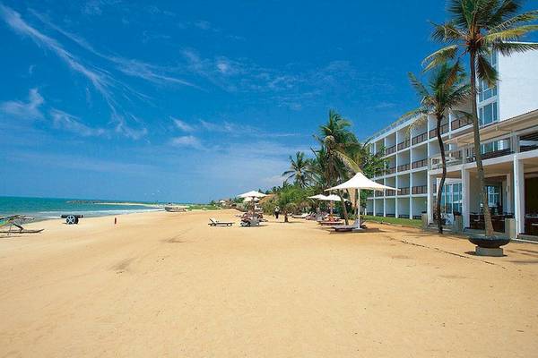 Strandansicht des Jetwing Sea Hotels mit weißen Sonnenschirmen und Liegestühlen.