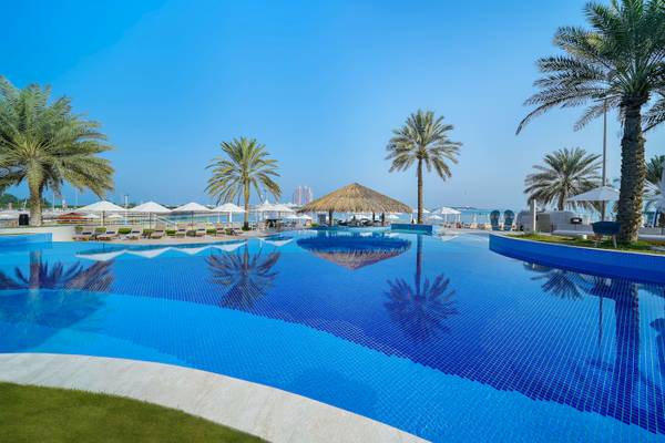 Poolbereich des Radisson Blu Hotel & Resort am Abu Dhabi Corniche mit Sonnenliegen und Palmen