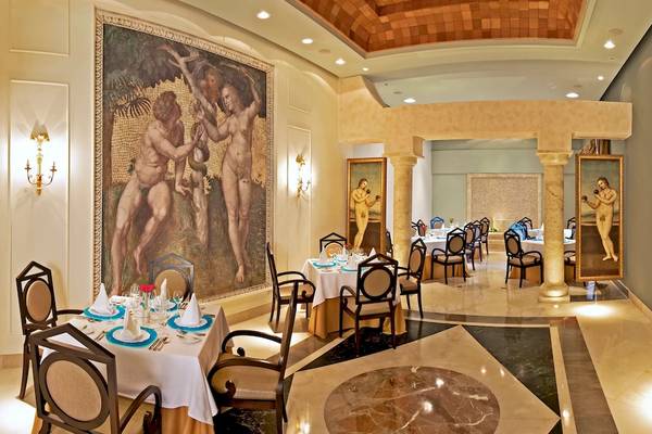 Der Innenbereich des JOIA Bávaro by Iberostar Hotels zeigt ein elegantes Restaurant mit Tischdecken, Stühlen und großen Gemälden an den Wänden.