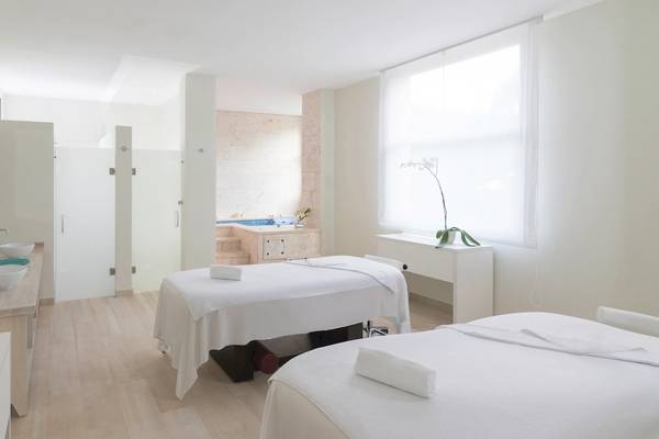Spa-Behandlungsraum im Hotel JOIA Bávaro by Iberostar mit zwei weißen Behandlungsliegen und einem Whirlpool im Hintergrund.