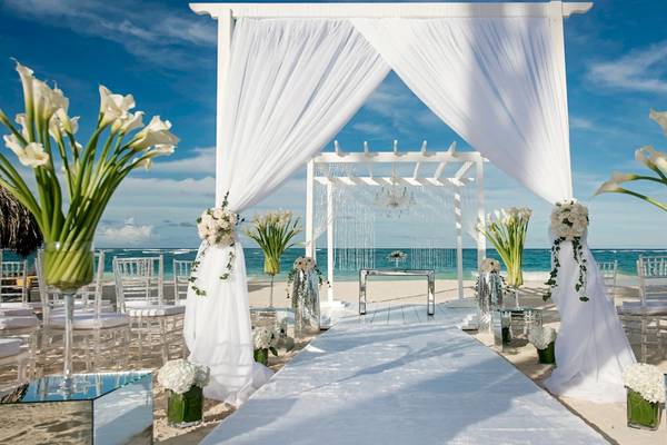Strandhochzeitszeremonie im JOIA Bávaro by Iberostar mit weißen Vorhängen und Blumen.