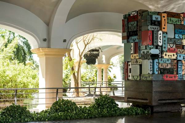 Eingangsbereich des Hotels JOIA Bávaro by Iberostar mit einer großen, bunten Koffer-Skulptur.