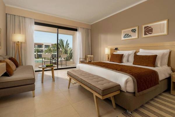 Ein elegantes Hotelzimmer im Jaz Elite Amara mit großem Bett, Schlafsofa, Tisch und Zugang zu einer Terrasse.