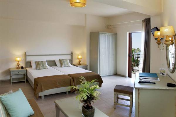 Doppelzimmer im Almyrida Beach Hotel mit zwei Betten, Nachttischen, einer Kommode, einer Lampe und einem offenen Balkon.