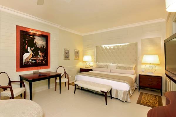 Suite-Schlafzimmer im JOIA Bávaro by Iberostar mit Doppelbett, Schreibtisch und Stühle.